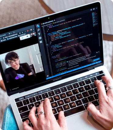 Pessoa digitando códigos em um notebook enquanto faz videochamada.